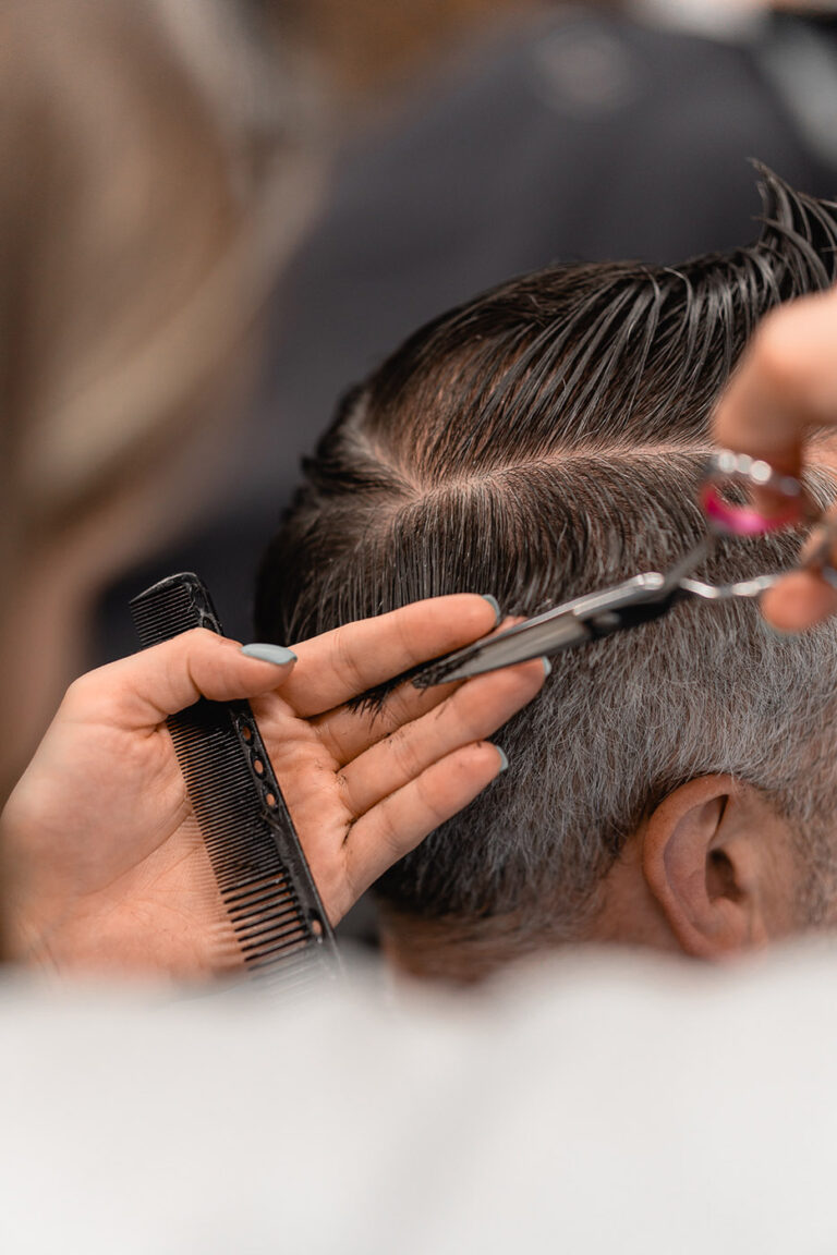 Barber wyczesuje pasmo na boku głowy i skraca włosy nożyczkami